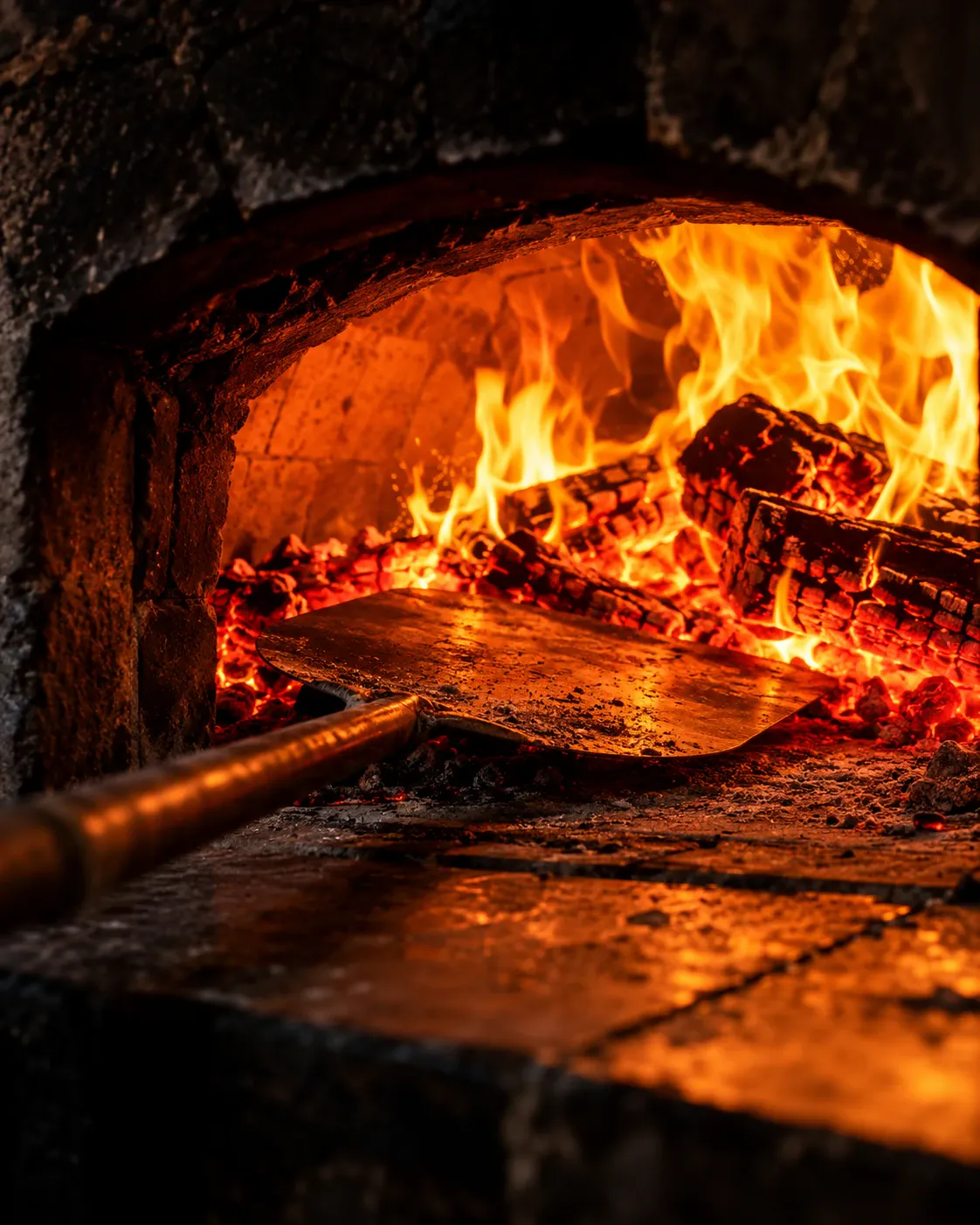 Pá entrando no forno a lenha, com a brasa e o fogo acesos
